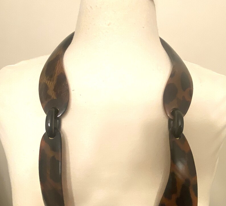 Peut inclure: Un long collier en plastique brun et noir avec un motif l&eacute;opard. Le collier est compos&eacute; de plusieurs pi&egrave;ces reli&eacute;es.