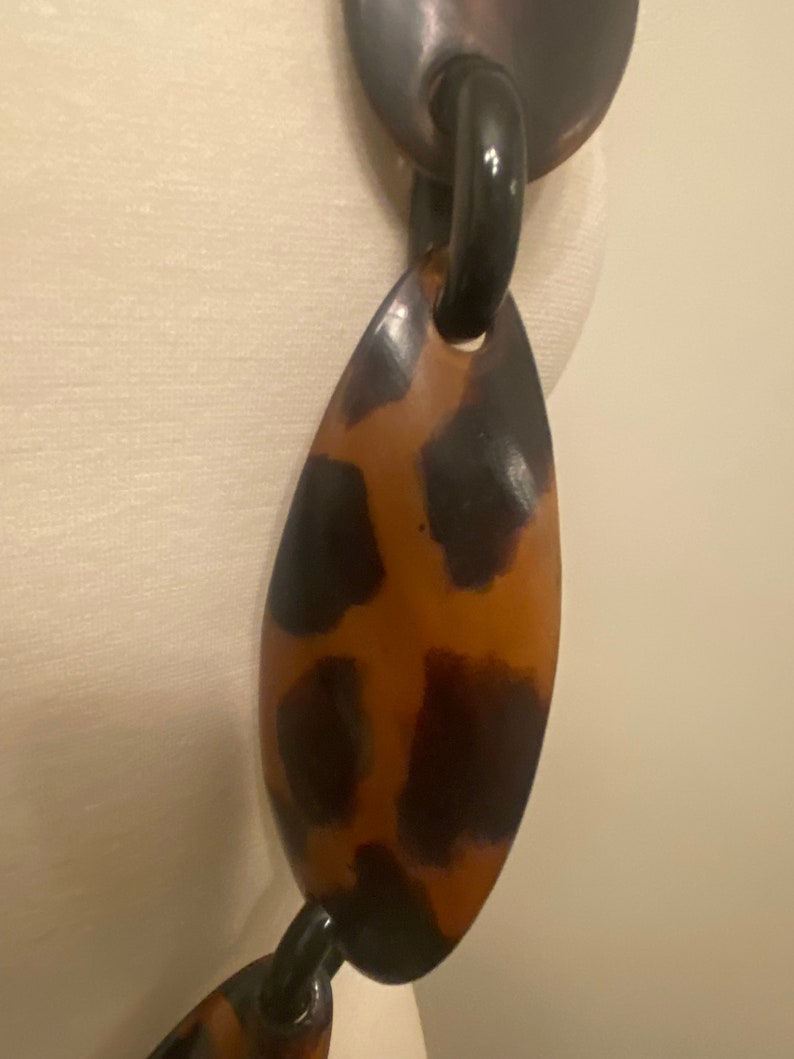 Peut inclure: Un collier &agrave; gros maillons ovales de couleur marron et noir. Le collier est en plastique et a une finition brillante.