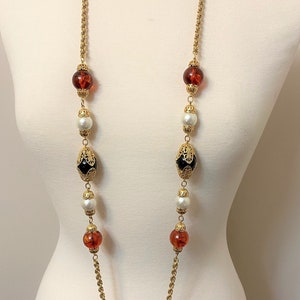 May include: A gold chain necklace with alternating amber, white pearl, and black glass beads. The beads are accented with gold filigree.