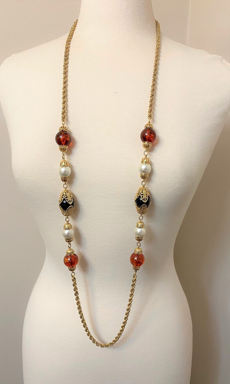 May include: A gold chain necklace with alternating amber, white pearl, and black glass beads. The beads are accented with gold filigree.