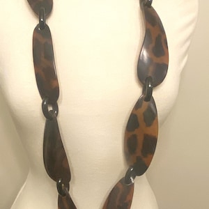 Peut inclure: Un long collier brun et noir avec des maillons de forme ovale. Les maillons ont un motif l&eacute;opard.