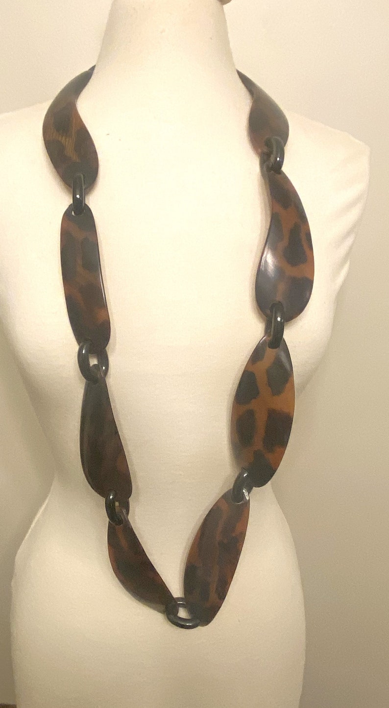 Peut inclure: Un long collier brun et noir avec des maillons de forme ovale. Les maillons ont un motif l&eacute;opard.