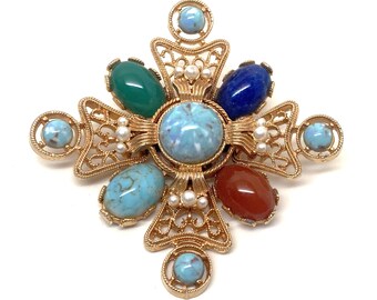 May include: A gold-coloured brooch in a cross design, decorated with colourful gemstones. The brooch has a large, light blue central stone, surrounded by smaller stones in green, blue, red, and turquoise. Small faux pearls add detail.