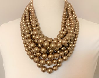 Peut inclure: Un collier de perles multi-rangs de couleur or. Le collier est composé de grosses perles rondes et est superposé pour créer un look épais et dramatique.