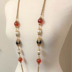 May include: A long gold chain necklace with alternating amber, white pearl, and black glass beads. The beads are set in gold.