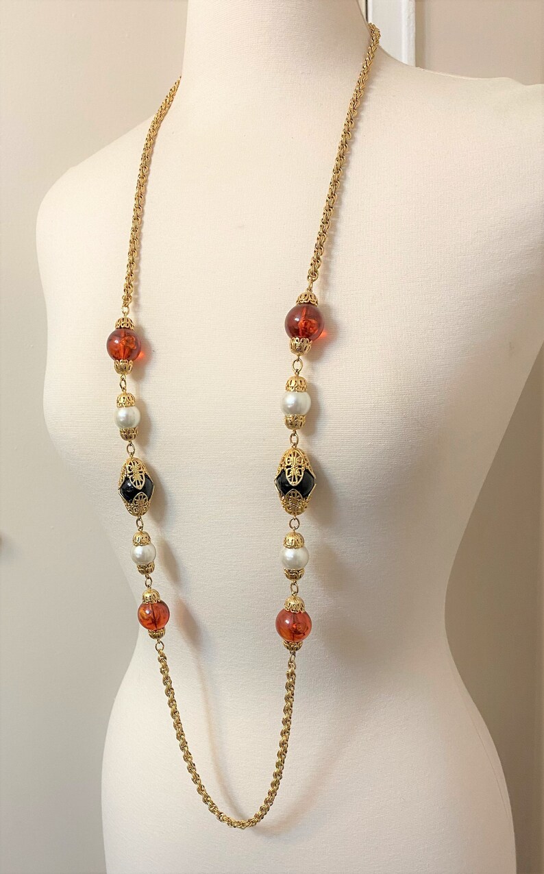 May include: A long gold chain necklace with alternating amber, white pearl, and black glass beads. The beads are set in gold.