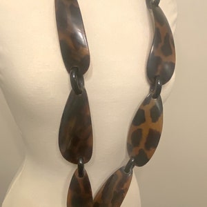 Peut inclure: Un long collier brun et noir avec un motif l&eacute;opard. Le collier est compos&eacute; de grandes pi&egrave;ces ovales reli&eacute;es par des anneaux noirs.