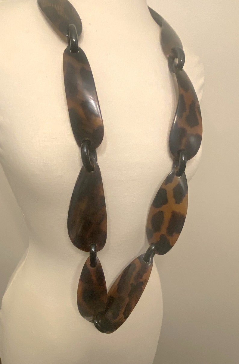 Peut inclure: Un long collier brun et noir avec un motif l&eacute;opard. Le collier est compos&eacute; de grandes pi&egrave;ces ovales reli&eacute;es par des anneaux noirs.