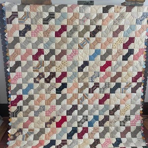 May include: A patchwork quilt featuring a repeating bow tie pattern in shades of red, blue, pink, and brown. The quilt has a scalloped edge and is displayed against a neutral backdrop. The design is a traditional handmade quilt.