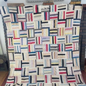 May include: A handmade quilt with a patchwork design. The quilt features rectangular blocks in various colors, including red, black, blue, and cream. The blocks are arranged in a grid pattern, creating a visually appealing and cozy textile.