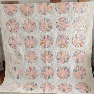 May include: A white ceramic mug with a black handle and the text "But First, Coffee" in a bold, black font. The mug is set against a blurred background, suggesting a cosy setting.