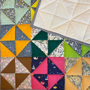 May include: A patchwork quilt featuring a mix of fabrics in blue, yellow, green, pink, and brown. The quilt has floral and nautical patterns, a white section, and a striped border. It is a handmade item, perfect for a bed or sofa.