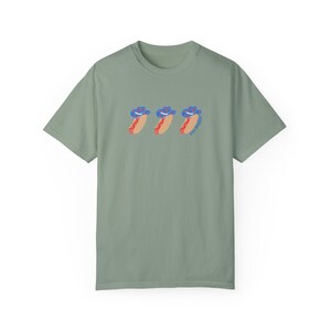 a green t-shirt with a graphic 3 hot dogs with red, white, and blue cowboy hats