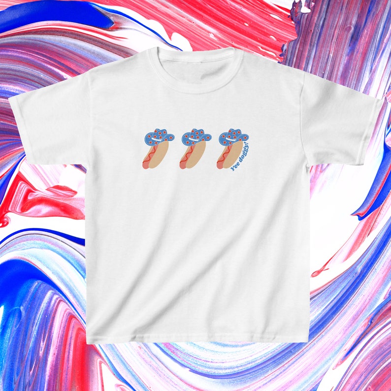 t-shirt with a graphic of 3 consecutively lined up hot dogs wearing red, white, and blue star-patterned cowboy hats, with the words “Yee doggy” in blue under the third hotdog in the center of the chest area