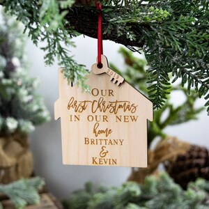 May include: A wooden house-shaped Christmas ornament with the text "Our first Christmas in our new home Brittany & Kevin" and the year "2019" engraved on it.