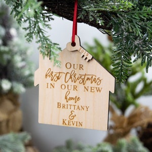 May include: A wooden Christmas ornament shaped like a house with the text "Our first Christmas in our new home Brittany & Kevin" and the year "2019" engraved on it.