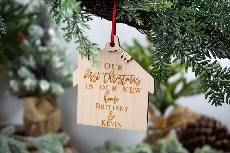 May include: A wooden Christmas ornament shaped like a house with the text "Our first Christmas in our new home Brittany & Kevin" and the year "2019" engraved on it.