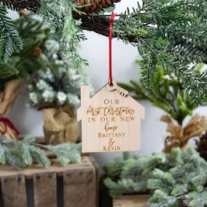 May include: A wooden house-shaped Christmas ornament with the text "Our first Christmas in our new home Brittany & Kevin".
