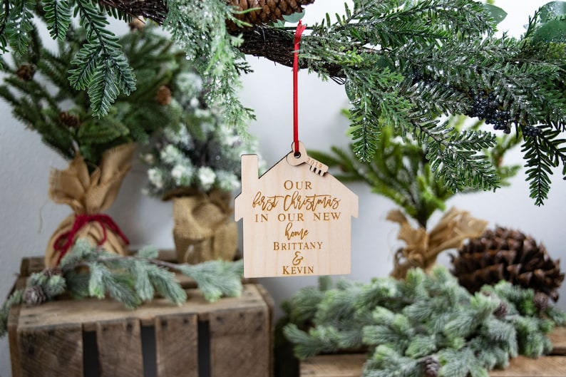May include: A wooden house-shaped Christmas ornament with the text "Our first Christmas in our new home Brittany & Kevin".