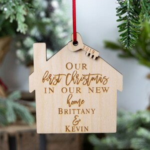 May include: A wooden Christmas ornament shaped like a house with the text "Our first Christmas in our new home Brittany & Kevin" and the year "2019" engraved on it.