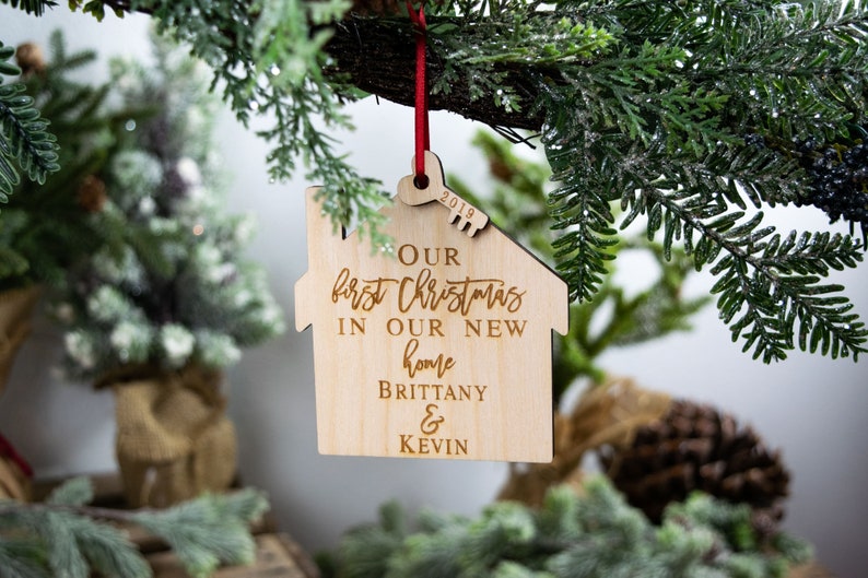 May include: A wooden house-shaped Christmas ornament with the text "Our first Christmas in our new home Brittany & Kevin" and the year "2019" engraved on it.