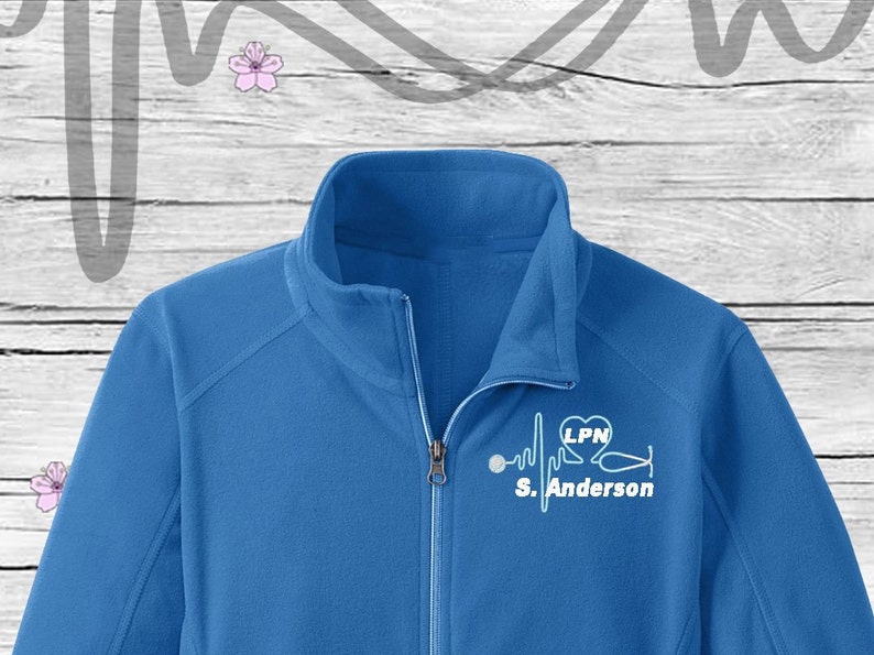 May include: A royal blue fleece jacket with a white embroidered design of a stethoscope, a heart with the letters LPN inside, and a heartbeat line with the name "S. Anderson" underneath.