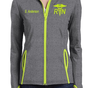 May include: A gray and neon green zip-up jacket with a caduceus and RN embroidered on the right side of the chest. The name "S. Anderson" is embroidered on the left side of the chest.