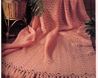May include: A crocheted throw blanket in a peach color with a fringe border. The blanket is made with a lacy stitch pattern.