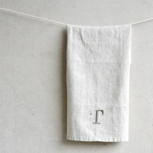 May include: A plain white linen kitchen towel with a single letter "T" embroidered in the centre.
