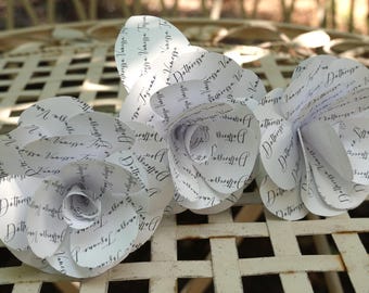 Könnte beinhalten: Nahaufnahme von drei weißen Papierblumen mit schwarzem Schrifttext. Die Blumen sind auf einer weißen, gitterartigen Oberfläche angeordnet. Der Text scheint ein Name zu sein: "Dottoressa Vanessa Toscana".