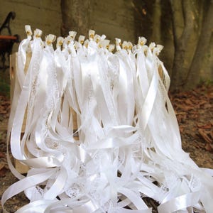May include: A collection of white ribbons with lace trim and gold accents, arranged in a wooden crate. The ribbons are of varying lengths and textures, creating a delicate and elegant display. Ideal for weddings or other special events.
