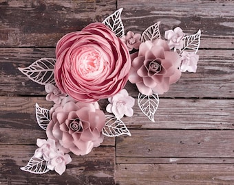 Puede incluir: Una colección de flores de papel rosa y blancas dispuestas sobre un fondo de madera rústica. Las flores están hechas de papel delicado y tienen un aspecto tridimensional en capas.