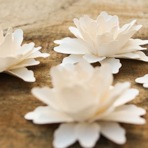 May include: Four white paper flowers with layered petals, arranged on a wooden surface.