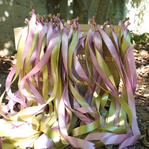May include: A collection of pink and gold satin ribbons tied to a wooden structure. The ribbons are arranged in a cascading pattern, with the ends of the ribbons resting on the ground. The ribbons are of varying lengths and widths, creating a visually appealing display.