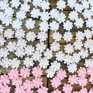 Op de afbeelding: Een houten oppervlak bedekt met witte en roze papieren bloemen. De bloemen zijn in rijen gerangschikt, met de witte bloemen bovenaan en de roze bloemen onderaan.