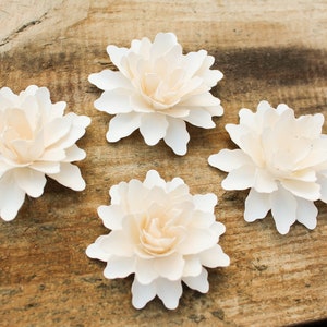May include: Four white paper flowers with a layered, ruffled design. The flowers are arranged on a wooden surface.