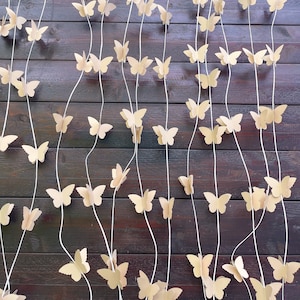 May include: A brown wooden wall with a string of beige paper butterflies hanging from it. The butterflies are evenly spaced and are all facing the same direction.