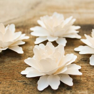 May include: Four white paper flowers with layered petals, arranged on a wooden surface.