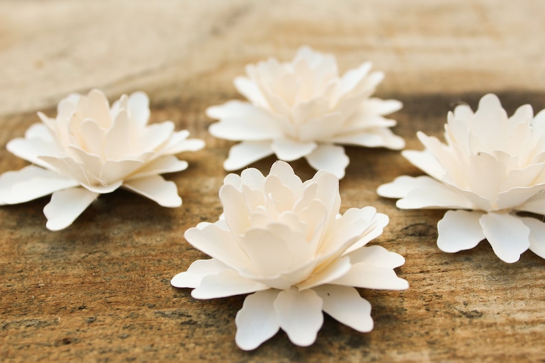 May include: Four white paper flowers with layered petals, arranged on a wooden surface.