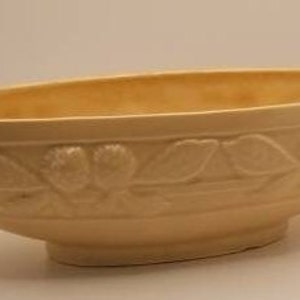 May include: A pale yellow ceramic bowl with an oval shape and a raised design of leaves and flowers around the rim.