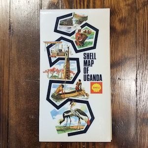 May include: A vintage Shell map of Uganda with illustrations of local wildlife and people. The map is surrounded by a blue border and features the Shell logo.