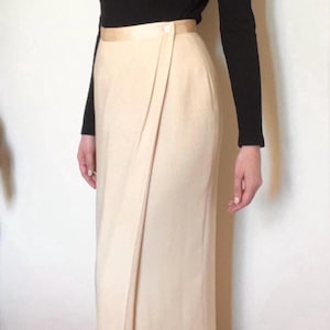 May include: A long-sleeved black top paired with a cream-colored wrap skirt. The skirt features a button closure at the waist and a draped design. The outfit is simple and elegant, suitable for various occasions.