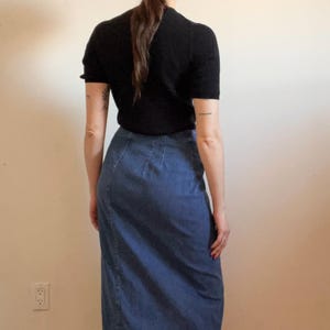 May include: A woman wearing a black short-sleeved shirt and a blue denim skirt.