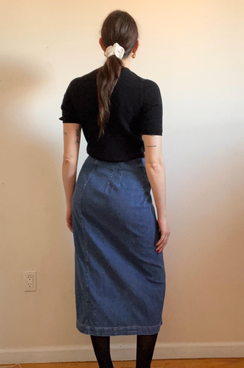 May include: A woman wearing a black short-sleeved shirt and a blue denim skirt.