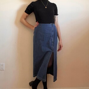 May include: A blue denim skirt with a front slit and a black mock neck shirt.