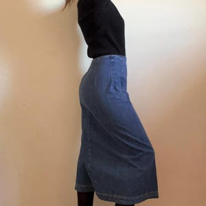 May include: A blue denim skirt with a straight, slightly flared silhouette. The skirt is knee-length and has a high waist.
