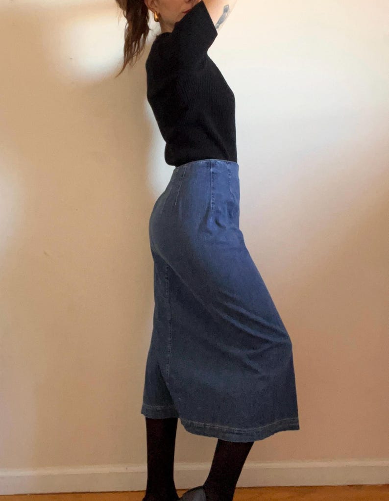 May include: A blue denim skirt with a straight, slightly flared silhouette. The skirt is knee-length and has a high waist.