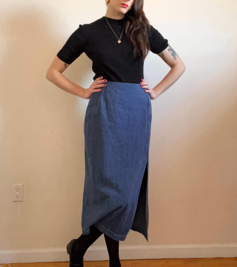 May include: A woman wearing a black mock neck shirt and a long blue denim skirt with a side slit.