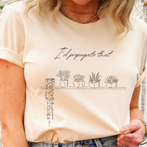 May include: A white t-shirt with the text "I'd propagate that" and a line drawing of potted plants on a shelf.
