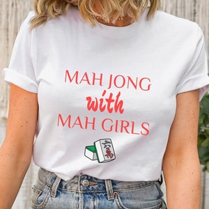 May include: White t-shirt with the text "Mah Jong with Mah Girls" in red. A small image of two mahjong tiles is below the text.